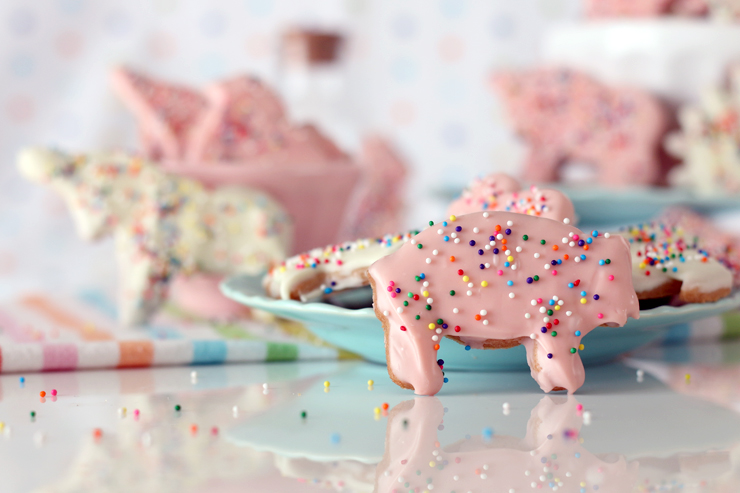 a pink pig animal cookie with rainbow sprinkles propped up to stand against a plate of animal cookies