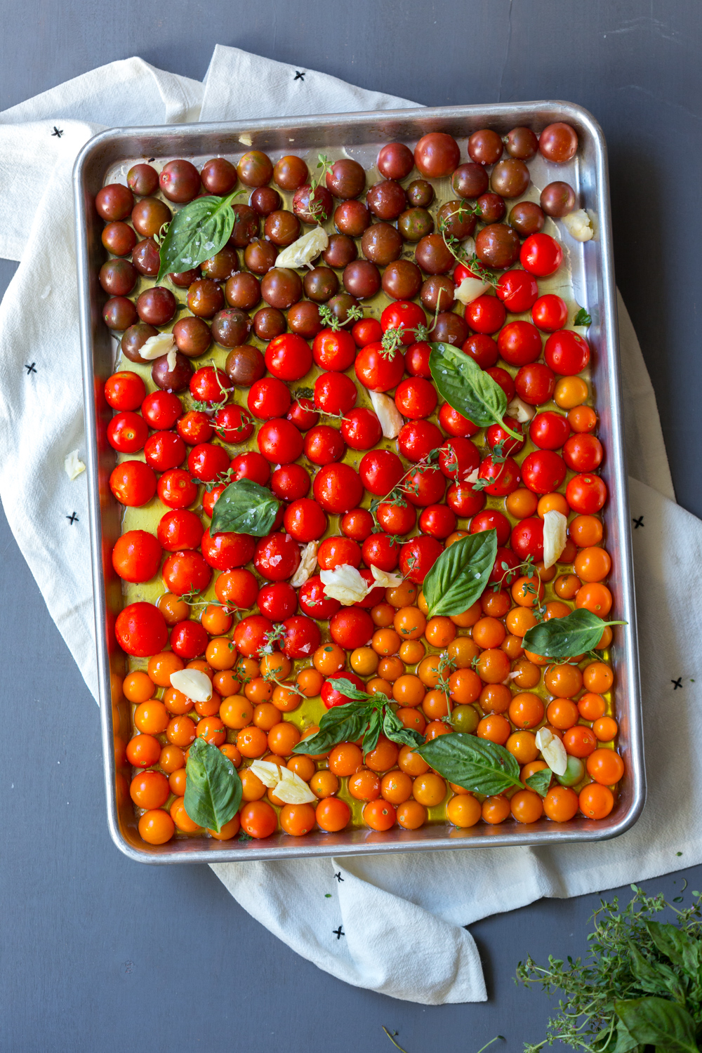 A prepared tray of cherry tomatoes with oil,  herbs, and garlic before baking