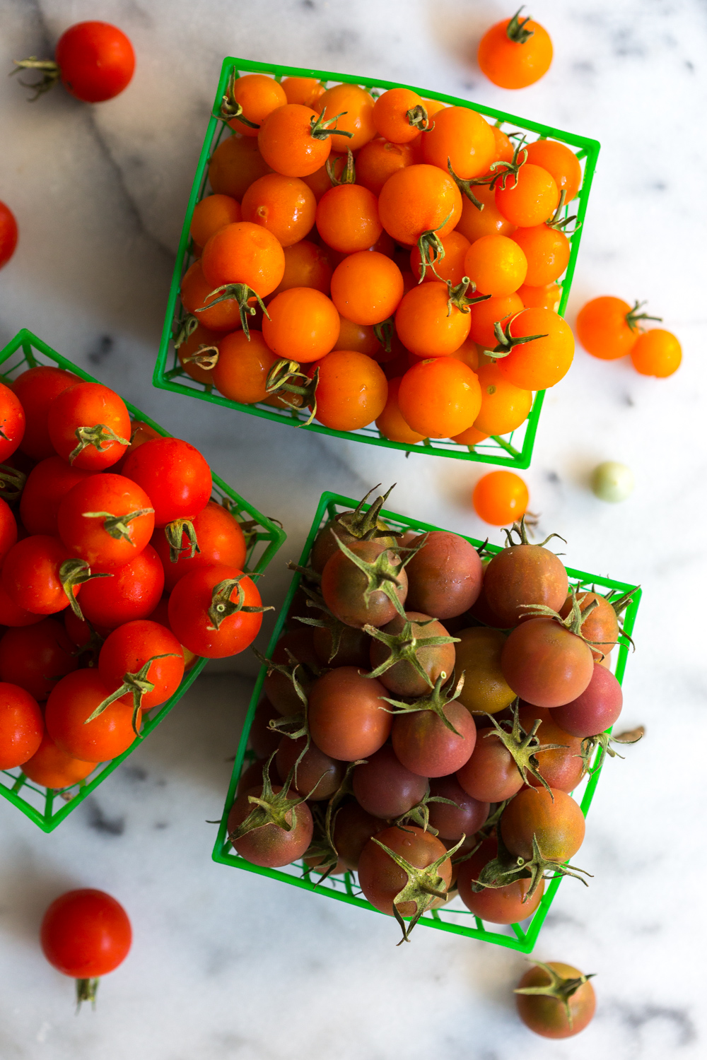 Red, orange, and dark cherry tomatoes in trays
